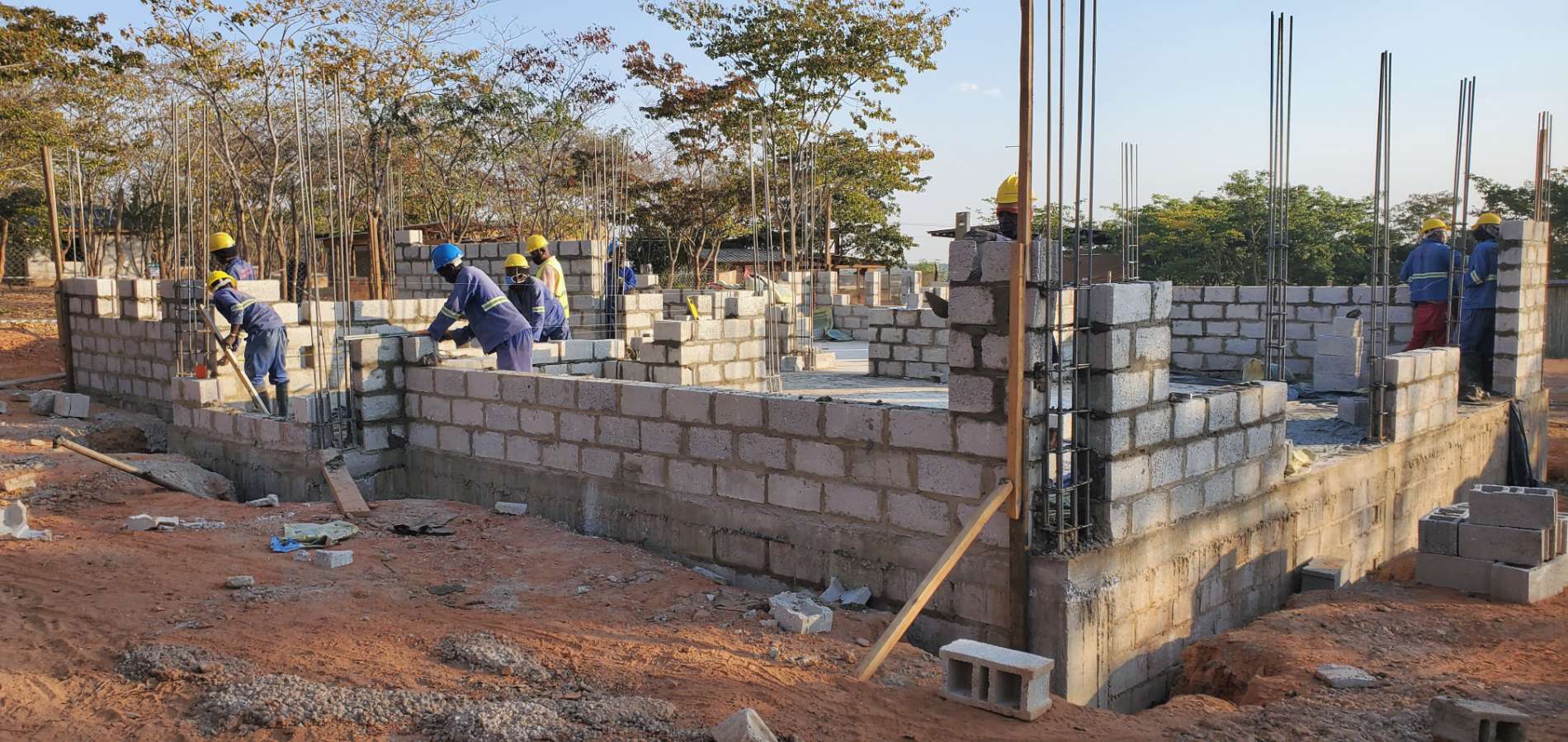Trainees in hard hats laying blockwork along the walls of the head office, reinforcement bars standing at the corners